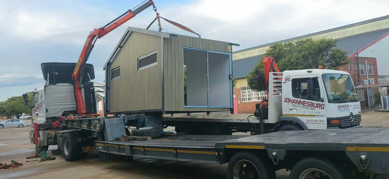 Johannesburg Truck and Crane Hire trucks lifting a modular building beside a lowbed trailer