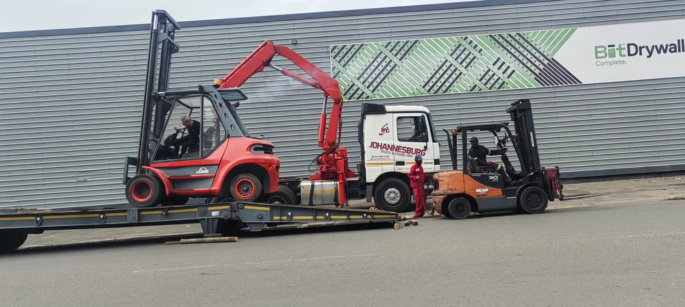 Forklift on a lowbed trailer alongside a branded Johannesburg Truck and Crane Hire truck